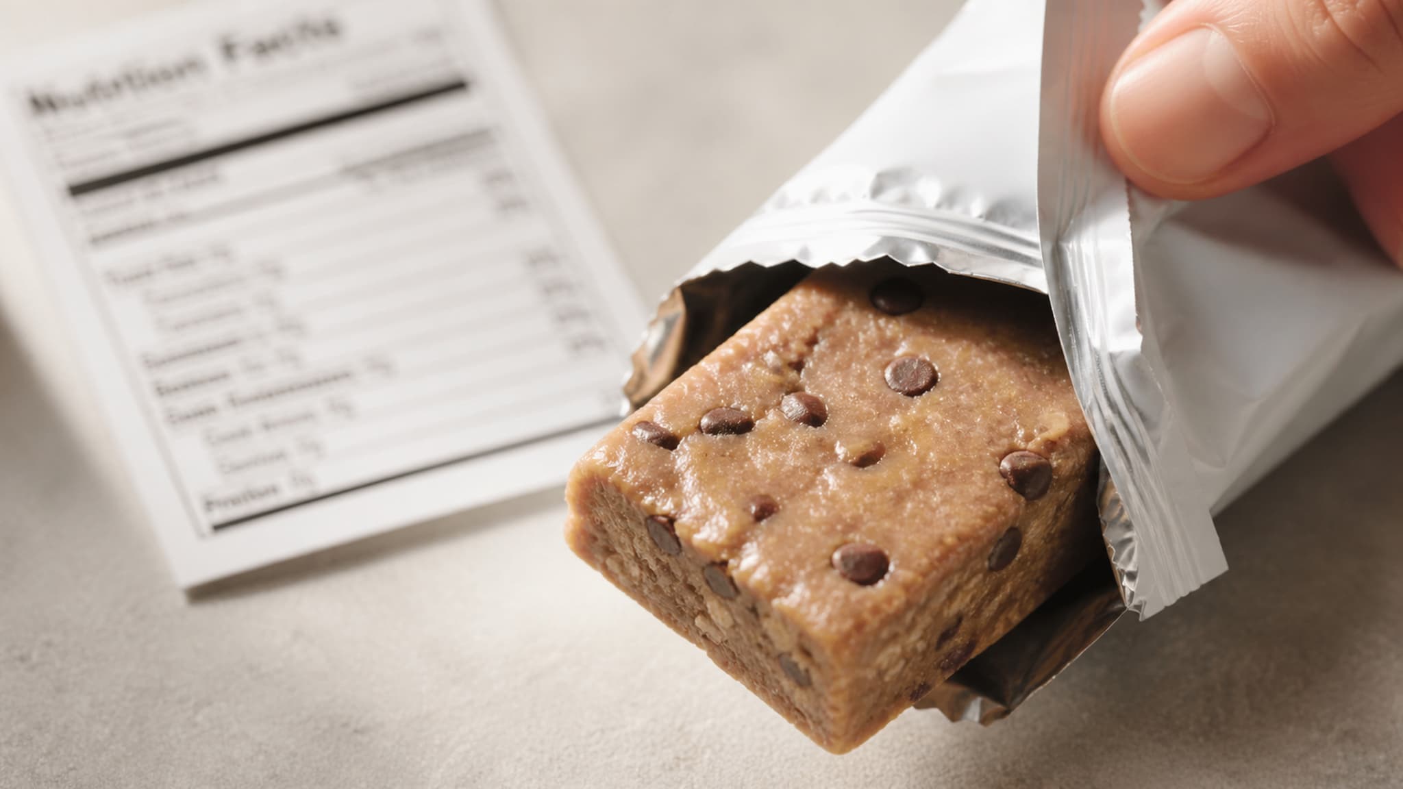 Close-up of a chocolate protein bar with visible peanuts, almonds, and chocolate chunks on a dark surface